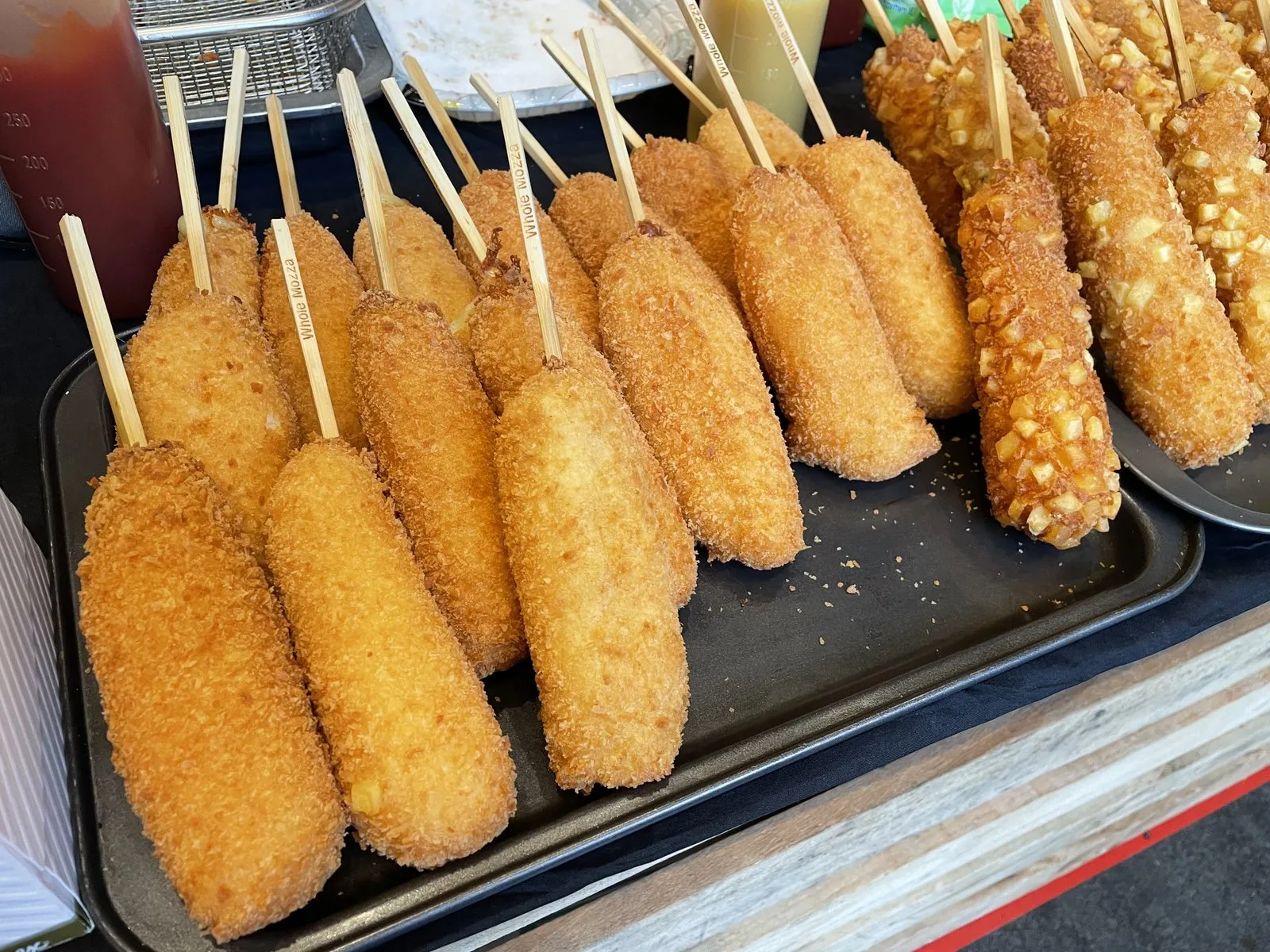 Corn dog Korea berbalut panko di atas tusuk kayu, digoreng keemasan dan ditaburi gula