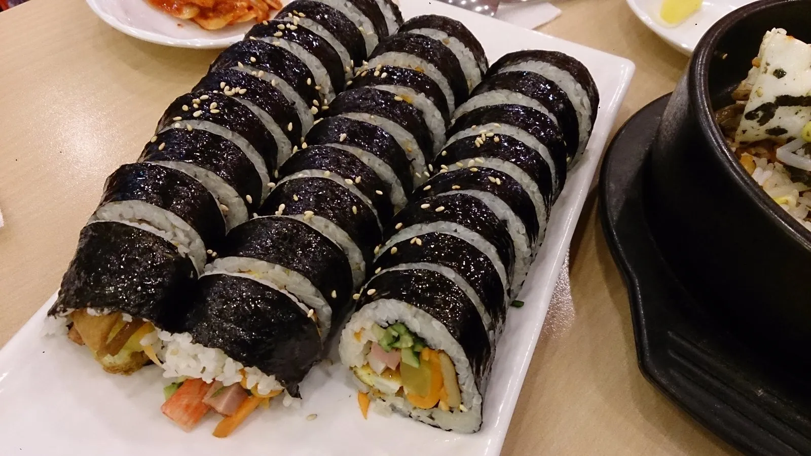 Irisan gulungan gimbap Korea dengan isian warna-warni berupa nasi, telur, wortel, bayam, dan acar lobak dalam lembaran rumput laut