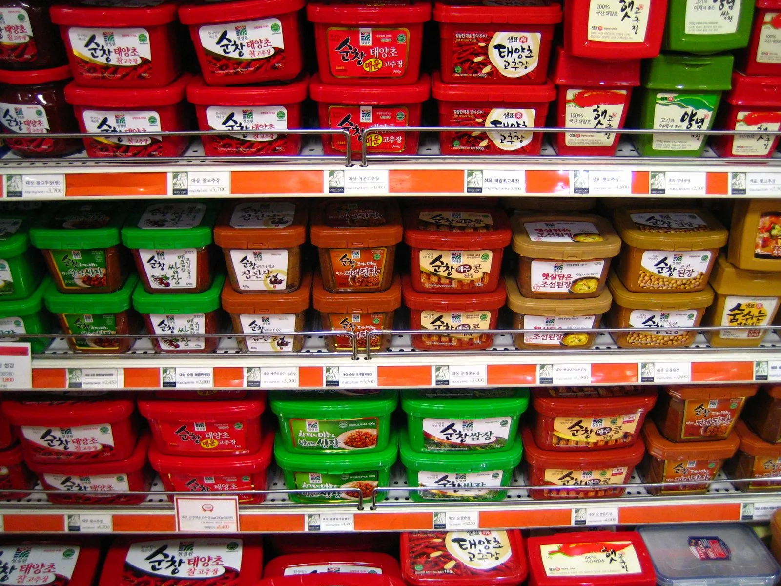 A Korean supermarket shelf stacked with red tubs of gochujang and other fermented soybean pastes, many of them the Sunchang brand